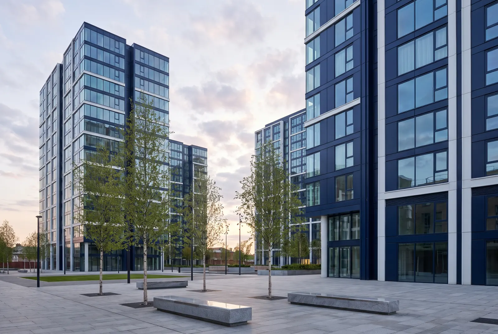 Glass residential towers above a small tree-lined plaza in early evening.