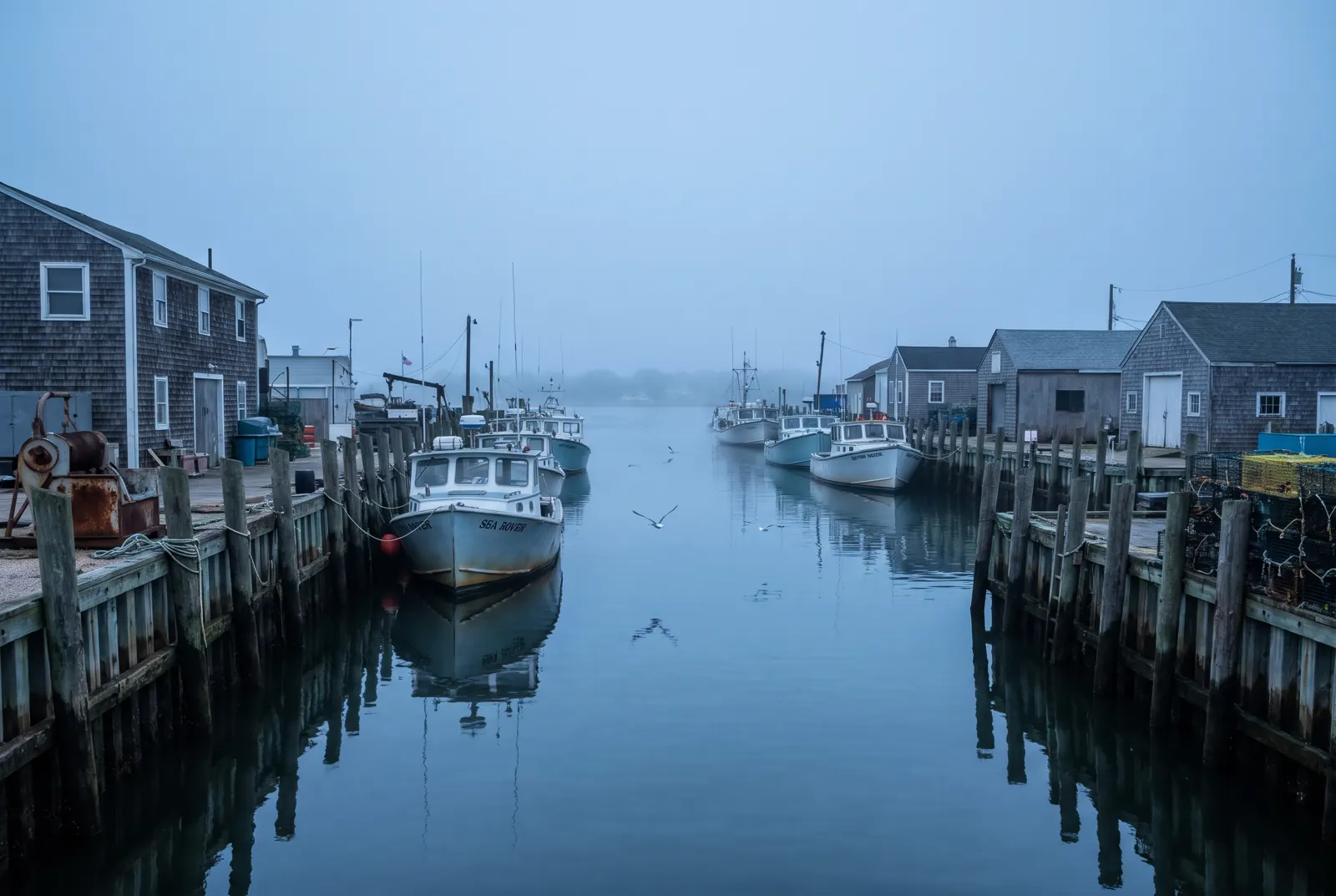 Fishing boats moored along a wooden bulkhead in a calm harbor channel at dawn