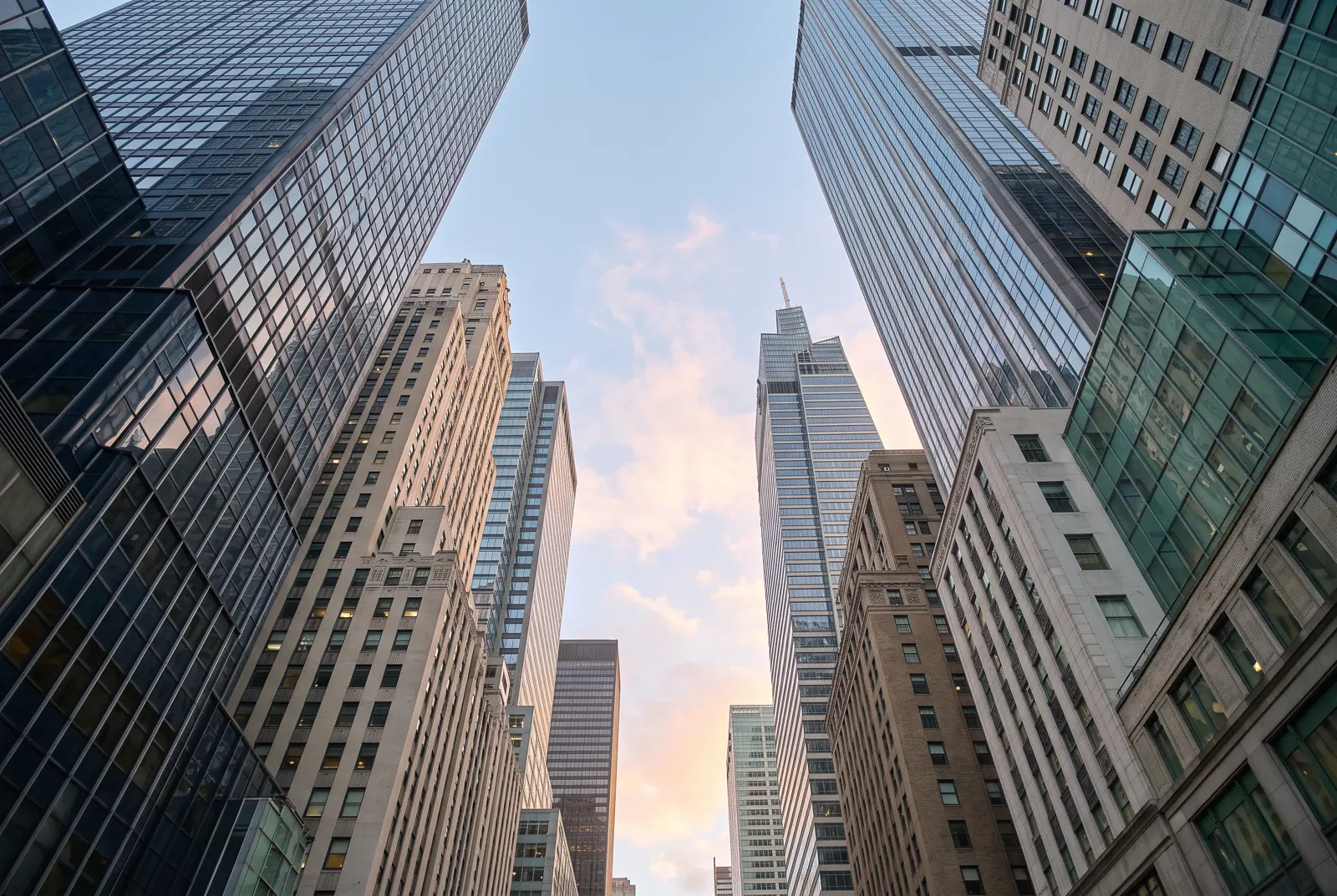 Tall skyscrapers seen from street level, their facades lit by dawn light.