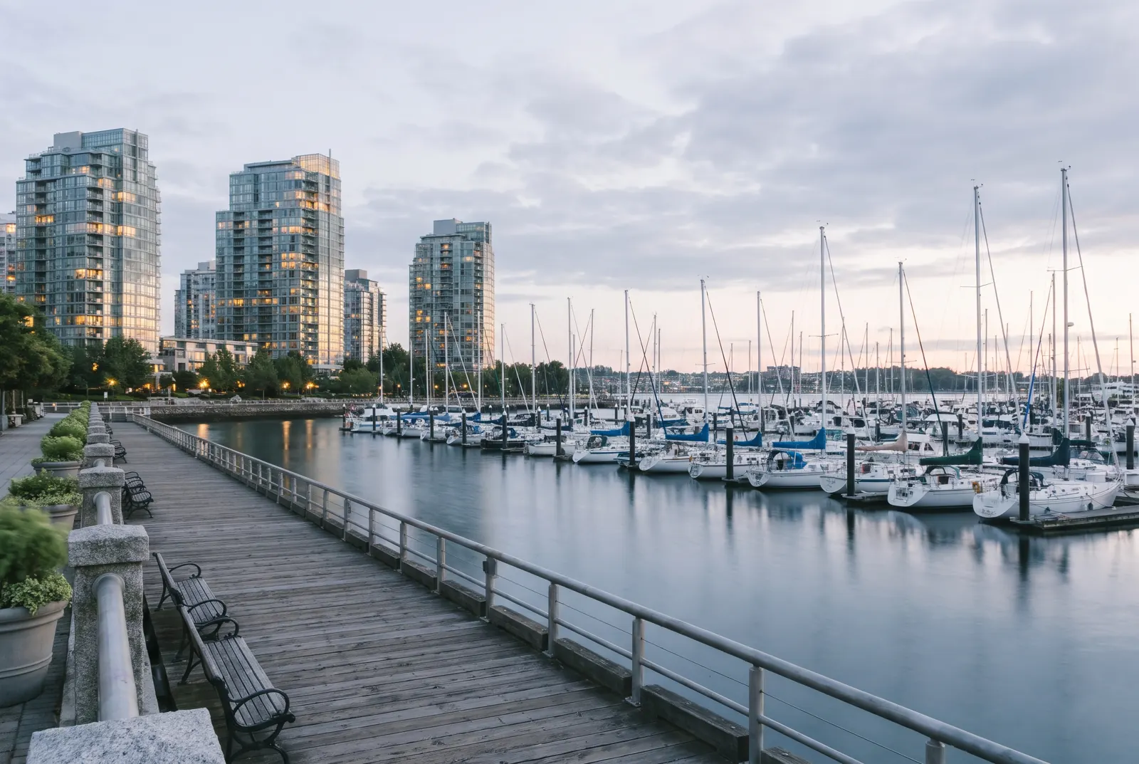 Sailboats in a calm marina at sunset with modern apartment towers along the far shore.